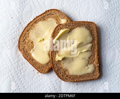 Vue de dessus de deux tranches de pain de blé légèrement grillé avec margarine sur des serviettes en papier blanc à la lumière naturelle. Banque D'Images