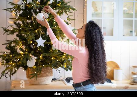 Bonne jeune femme décorant l'arbre de Noël à la maison dans la cuisine intérieur Banque D'Images