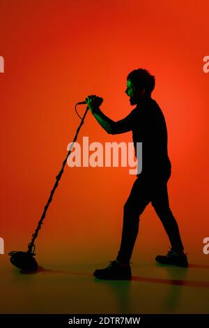 Expressif. Silhouette de jeune guitariste mâle isolée sur fond orange gradient studio au néon. Des ombres magnifiques en action, en action. Concept des émotions humaines, de l'expression, de la publicité, de la musique, de l'art. Banque D'Images