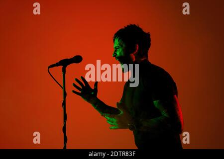 Expressif. Silhouette de jeune guitariste mâle isolée sur fond orange gradient studio au néon. Des ombres magnifiques en action, en action. Concept des émotions humaines, de l'expression, de la publicité, de la musique, de l'art. Banque D'Images
