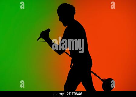 Étape. Silhouette de jeune guitariste mâle isolée sur fond de studio de gradient vert-orange au néon. Des ombres magnifiques en action, en action. Concept des émotions humaines, de l'expression, de la publicité, de la musique, de l'art. Banque D'Images