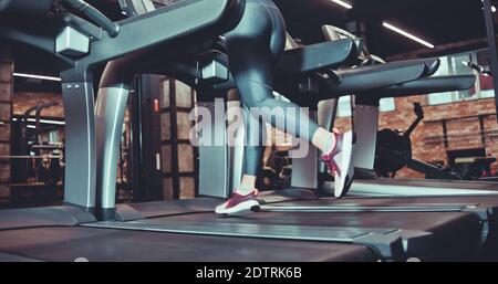 Pieds musclés féminins dans des baskets et des leggins qui s'exécutent sur le pied de la salle de sport. Entraînement cardio Banque D'Images