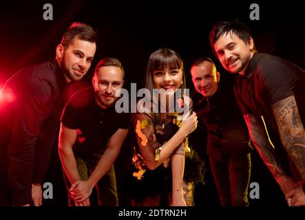 Jeunes. Portrait de groupe de musicien isolé sur fond sombre de studio en lumière néon. De magnifiques modèles caucasiens qui se comportent de la même qualité émotionnelle. Concept des émotions humaines, expression faciale, publicité, musique, art. Banque D'Images