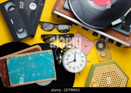 Attributs rétro, médias des années 80. Lecteur de vinyle, cassettes vidéo, cassettes audio, lunettes 3d, disques, radio, réveil d'époque, vieux livres sur une bande jaune Banque D'Images