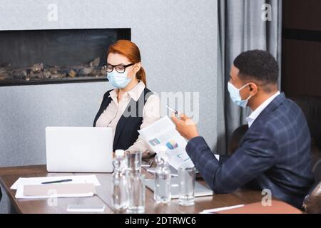 Homme d'affaires afro-américain avec un document pointant avec un stylo en position assise près d'une femme d'affaires sur le lieu de travail Banque D'Images