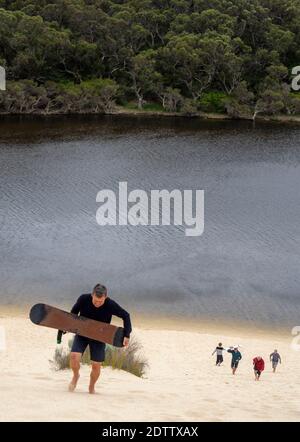 Des hommes grimpant sur une dune de sable pour faire du surf sur la rivière Moore Guilderton, en Australie occidentale. Banque D'Images