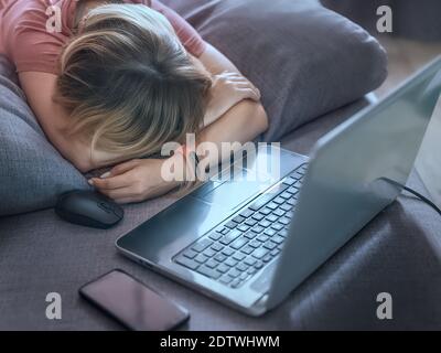 Une fille célibataire dormant sur le canapé avec un ordinateur portable et un smartphone en face d'elle. Fatigue, surcharge de travail, dépendance à Internet et auto-isolement t Banque D'Images
