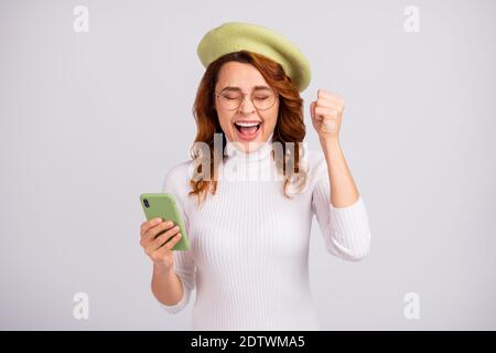 Portrait d'une jeune fille aux cheveux ondulés plutôt joyeuse tenant à la main cellule se réjouissant isolée sur fond gris clair blanc Banque D'Images