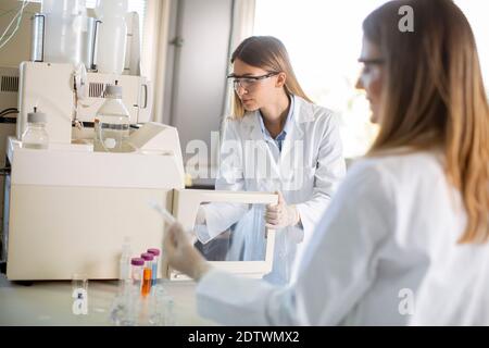 Jeunes femmes scientifiques dans un flacon de mise en blouse de laboratoire blanc avec un échantillon pour une analyse sur un système d'ionchromatographie en laboratoire biomédical Banque D'Images