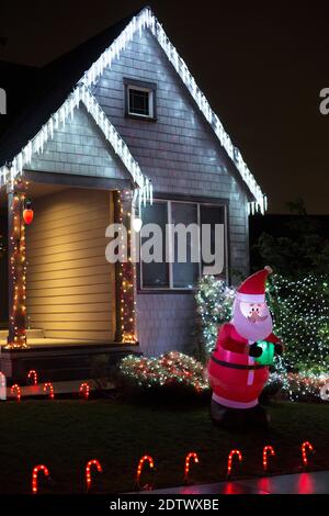 Une maison décorée pour Noël avec des lumières et un Père Noël gonflable sur la pelouse, la nuit. Banque D'Images