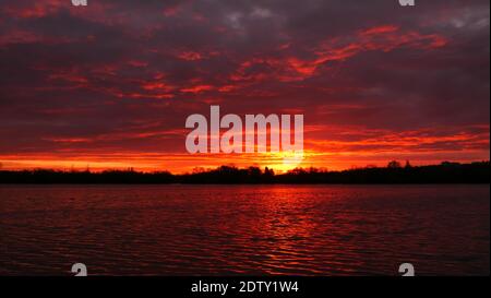 Un lever ou un coucher de soleil incroyable sur un lac. Ciel rouge spectaculaire à l'horizon avec de l'eau au premier plan. Banque D'Images