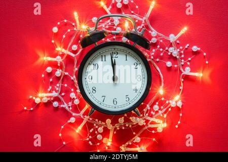 Le Garland s'illumine autour d'un réveil d'époque à minuit. Horloge à la nuit du nouvel an sur fond rouge. Douze heures, Noël et le nouvel an fesent Banque D'Images