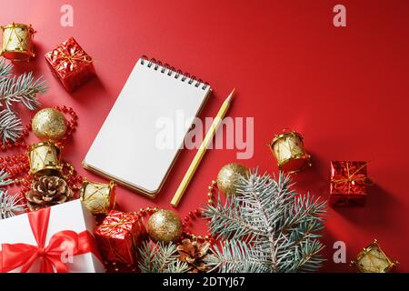 Bloc-notes et crayon pour écrire des voeux et des cadeaux pour le nouvel an et Noël autour des décorations d'arbre de Noël sur un fond rouge. Nouvel an moo Banque D'Images