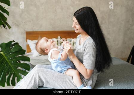 Maman s'assoit au lit et tient soigneusement le bébé dans ses bras. Le nouveau-né sourit dans les bras de sa mère. Banque D'Images