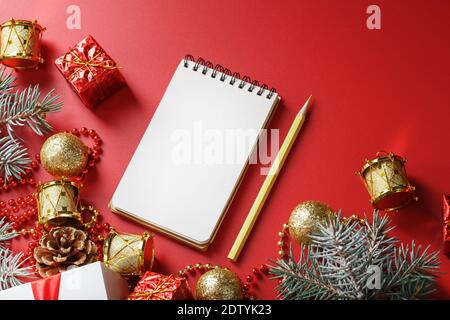 Bloc-notes et crayon pour écrire des voeux et des cadeaux pour le nouvel an et Noël autour des décorations d'arbre de Noël sur un fond rouge. Nouvel an moo Banque D'Images