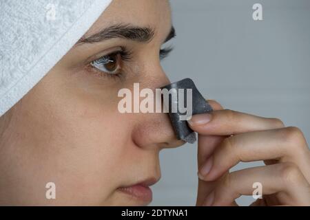 Une femme enlève une bande de nettoyage de son nez. Points noirs sur le nez. Fille sans maquillage dans la salle de bains. Soins de la peau, problèmes de peau, nettoyage. Natu Banque D'Images