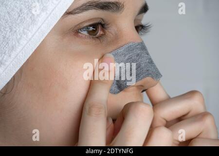 Une femme colle une bande de nettoyage sur son nez. Points noirs sur le nez. Fille sans maquillage dans la salle de bains. Soins de la peau, problèmes de peau, nettoyage. Naturel Banque D'Images