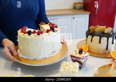 Gros plan de la femme mettant le gâteau sucré aux baies sur la table à d'autres desserts Banque D'Images