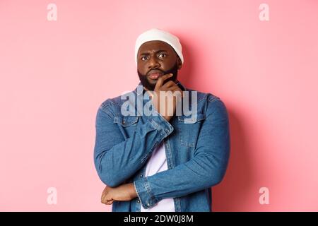 Homme afro-américain doué, regardant la caméra avec incrédulité, se tenant sceptique et pensant, fond rose Banque D'Images