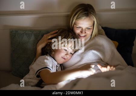 Mère et fils utilisant une tablette numérique ensemble la nuit lit Banque D'Images