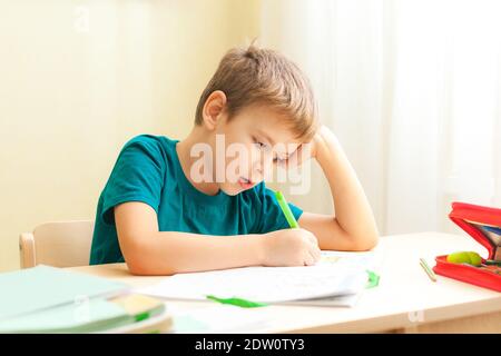 7 yeas vieux garçon assis à un bureau et faisant des devoirs. L'enfant écrit des notes dans le carnet, les devoirs difficiles, l'enfant se concentrant sur des exemples Banque D'Images