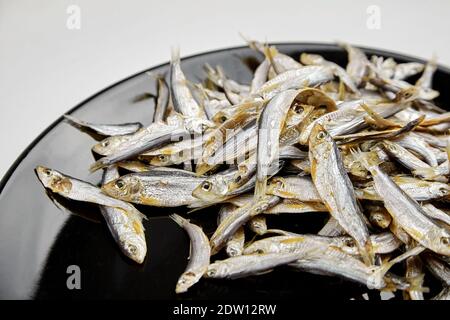 Petit poisson salé séché sur fond d'assiette noire. Encas à la bière. Banque D'Images