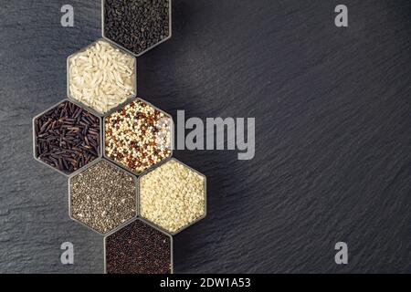 Différentes céréales et grains dans les pots en nid d'abeille de forme hexagonale sur une surface en pierre noire Banque D'Images