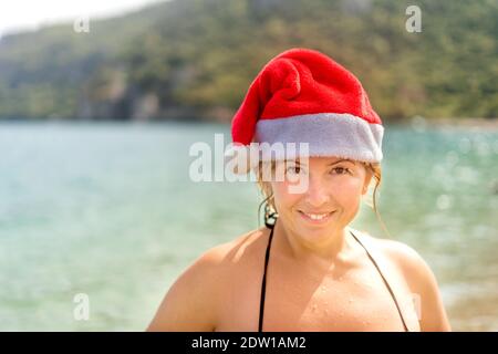 Vue rapprochée de la femme caucasienne souriante en maillot de bain et chapeau du Père Noël sur la plage tropicale. Vue rapprochée. Espace pour le texte. Banque D'Images