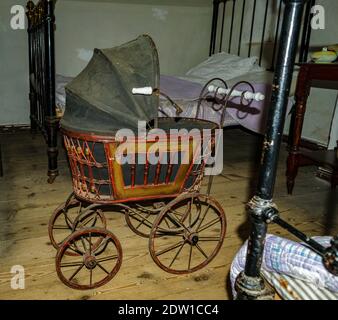 Poussette ancienne vintage pour bébé dans une chambre sombre de style ancien, avec deux lits anciens et des couvertures Banque D'Images