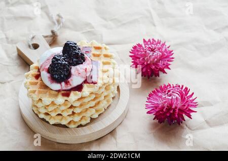 Biscuits de gaufre à la crème aigre et aux mûres confites sur une planche en bois. Fond en papier froissé et fleurs cramoisi Banque D'Images