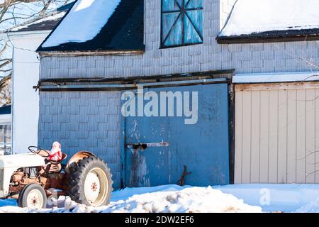 Jouet Santa Claus assis sur un tracteur de ferme en face d'une ancienne grange en bois délabrée. Banque D'Images