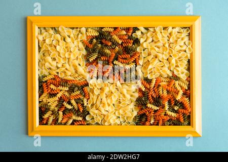 pâtes de tarière colorées et pâtes de papillons à la tonde farfalle sur fond bleu clair texturé dans un cadre en bois jaune abstrait, macaroni. pâtes de légumes Banque D'Images