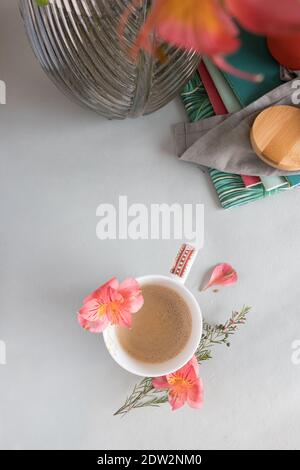 Vue en hauteur d'une tasse de café mousseuse à côté d'un vase avec des fleurs et quelques blocs-notes empilés. Banque D'Images