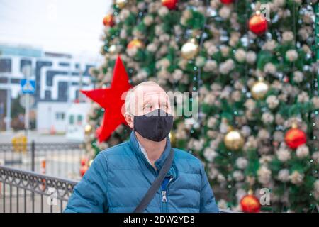 Homme adulte dans un masque de protection contre le fond d'un arbre de Noël festif. Célébration de Noël et du nouvel an pendant la pandémie du coronavirus. Banque D'Images