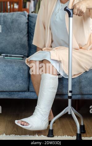 La femme d'âge moyen avec une jambe cassée est assise sur le canapé à la maison Banque D'Images