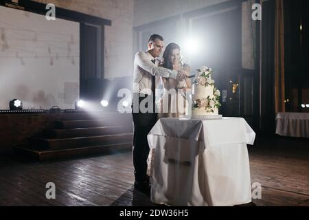 Heureux newlyweds coupant trois niveaux gâteau de mariage décoré avec des fleurs. Fête de mariage. Mariée et marié souriants Banque D'Images
