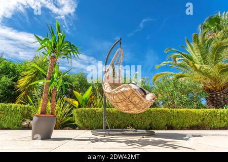 Chaise pivotante suspendue pour se détendre dans un jardin de luxe, vue sur le fond avec un pot de fleurs. Banque D'Images