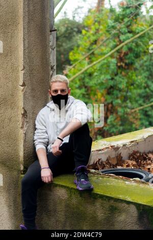 Un jeune homme blond assis sur une bordure de fenêtre d'un maison abandonnée Banque D'Images