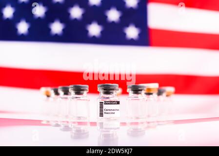 Flacons médicaux avec le vaccin Covid et une seringue, devant un drapeau américain non focalisé. Banque D'Images