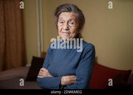 Vieille grand-mère caucasienne âgée de quatre-vingt-dix ans regarde attentivement et sourit, se sent heureuse, grand portrait, visage avec des rides profondes, cheveux gris. T Banque D'Images