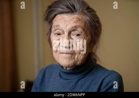 Vieille grand-mère caucasienne âgée de quatre-vingt-dix ans regarde attentivement et sourit, se sent heureuse, grand portrait, visage avec des rides profondes, cheveux gris. T Banque D'Images