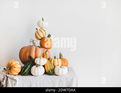 Citrouilles colorées de différentes formes et tailles en pyramide sur nappe légère, mur blanc à l'arrière-plan, espace de copie. Citrouilles pour la région de Hallowee Banque D'Images