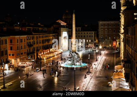 Vue sur la Piazza Navona la nuit avec des cafés illuminés et la fontaine des quatre rivières de Bernini illuminée pendant que les touristes aiment la soirée. Banque D'Images