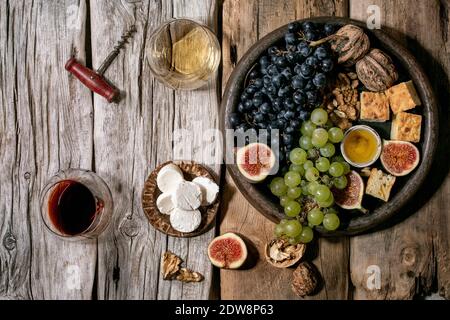 Hors-d'œuvre au vin avec différents raisins, figues, noix, pain, miel et fromage de chèvre sur plaque en céramique, servant avec des verres de vin rouge et blanc sur o Banque D'Images