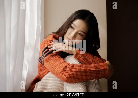 Dépression triste fille se sentant seule assis à la maison hiver regardant par la fenêtre en hiver temps froid. Femme asiatique se sentant malheureuse. Concept de dépression, solitude, anxiété, émotions de douleur Banque D'Images