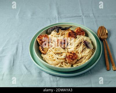 Boulettes de parmesan courgettes aux pâtes Carbonara dans une assiette verte sur une nappe bleue. Vue rapprochée de la carbonara crémeuse avec espace de copie Banque D'Images