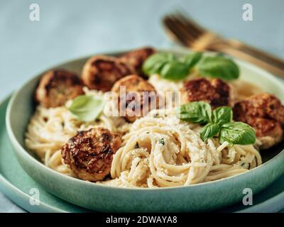 Boulettes de parmesan courgettes aux pâtes Carbonara dans une assiette verte sur une nappe bleue. Vue rapprochée de la carbonara crémeuse avec boulettes de viande de bœuf. Banque D'Images