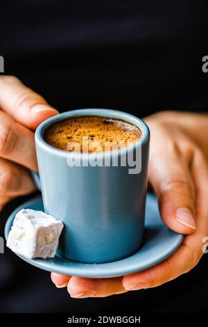 Femme avec un chandail noir tenant un café turc dans une tasse de café gris, un délice turc sur le côté. Banque D'Images