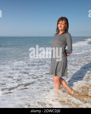 Femme debout dans une robe sur le bord de mer lavé par les vagues Banque D'Images