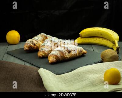 Croissant avec garniture de fruits comme fond. Croissant frais et croustillant sur un plateau en pierre. Vue latérale Banque D'Images